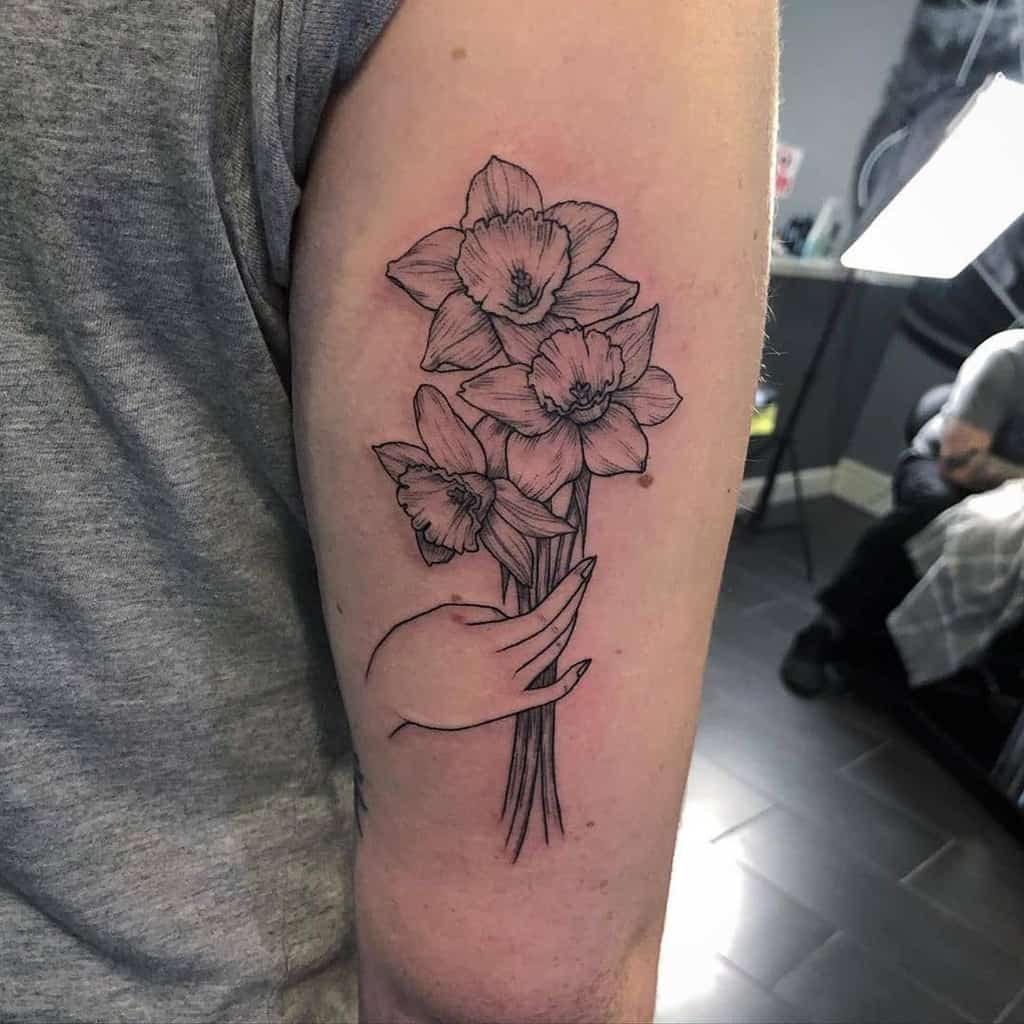 Tattoo of a daffodil flower and arm on the shoulder for men