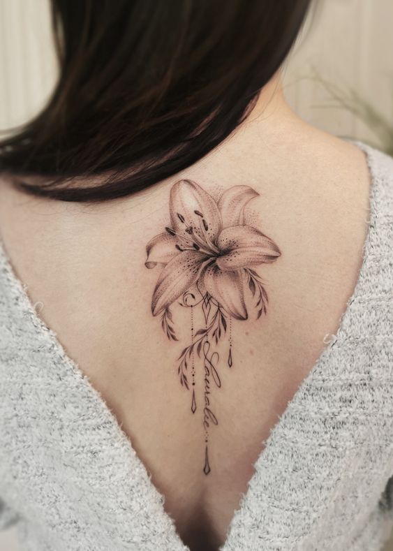 Lily tattoo with an inscription on the spine for women