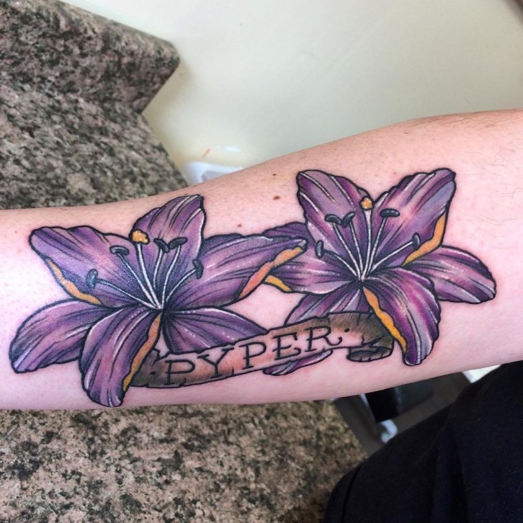 Colorful tattoo of two lilies with an inscription on the arm for women