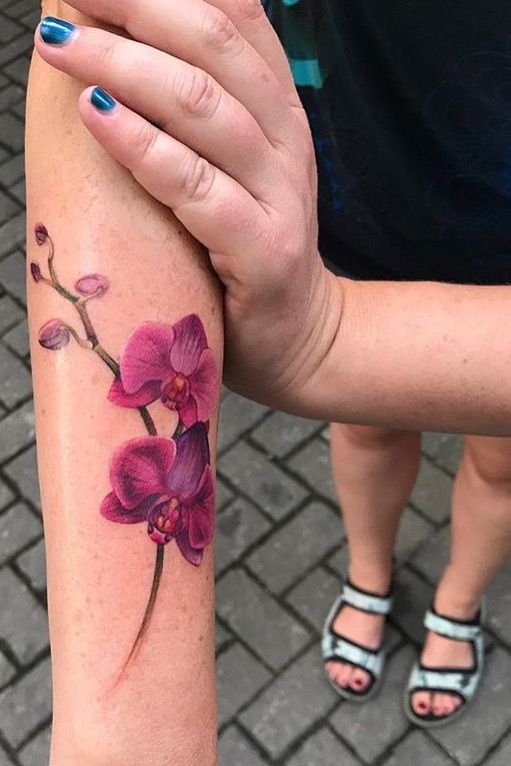 Color tattoo of an orchid on the forearm for women