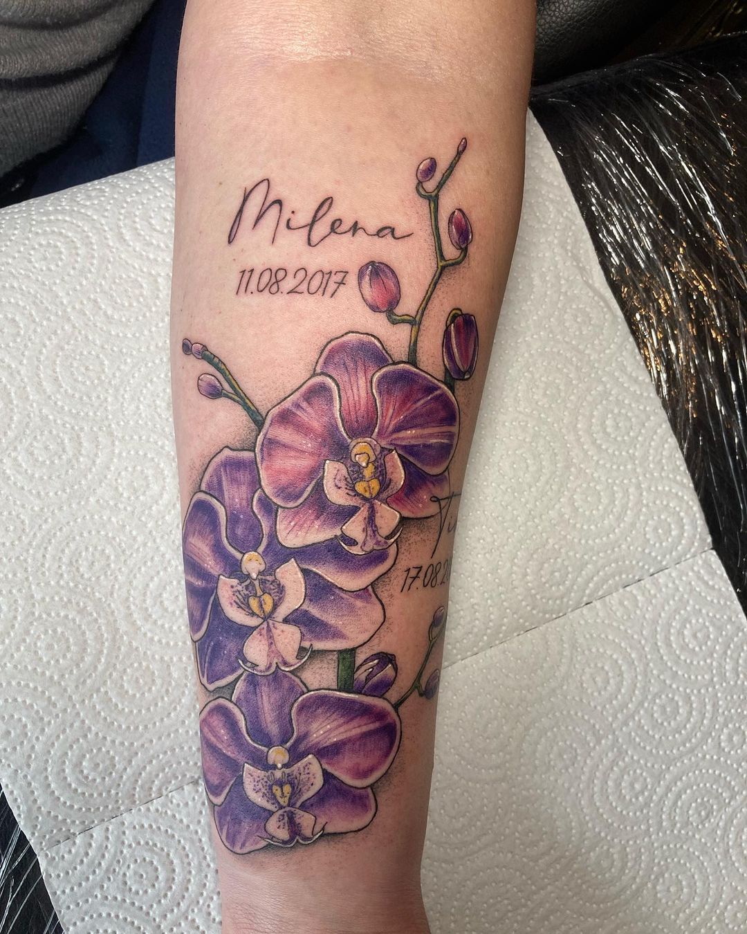 Color tattoo of an orchid with an inscription on the forearm for women