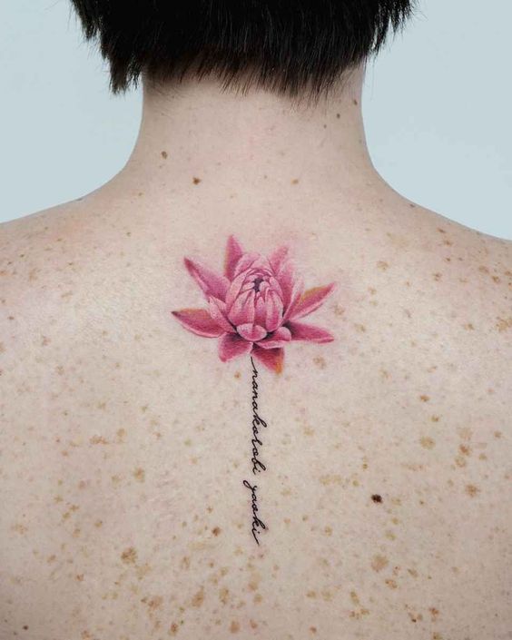 Colored lotus tattoo with inscription on the spine for women