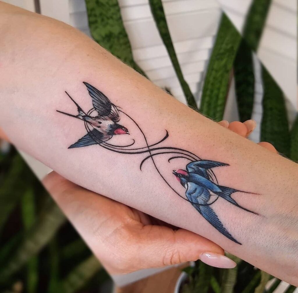 Colorful tattoo of two swallows with the infinity sign on the hand for women