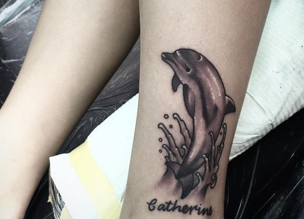 Large dolphin tattoo with inscription on the shin for women