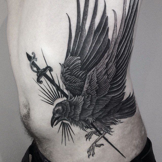 Large tattoo of a raven with a dagger on the side for men