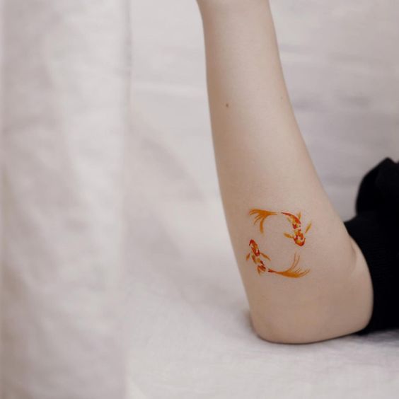 Colorful tattoo of three goldfish on the arm for women