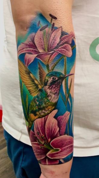 Large hummingbird tattoo with lilies on the forearm for men