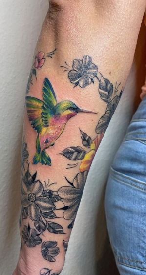 Color tattoo of a hummingbird with flowers on the forearm for women