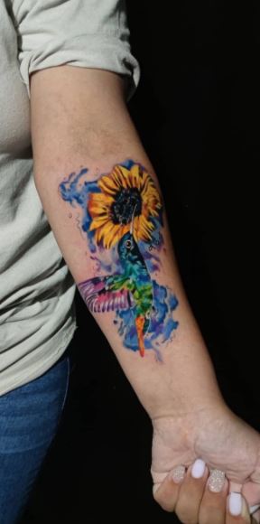 Color tattoo of a hummingbird with a sunflower on the forearm for women