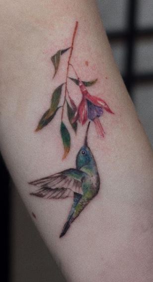 Color tattoo of a hummingbird with a flower on the arm for women