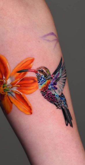 Color tattoo of a hummingbird with a lily on the forearm for women