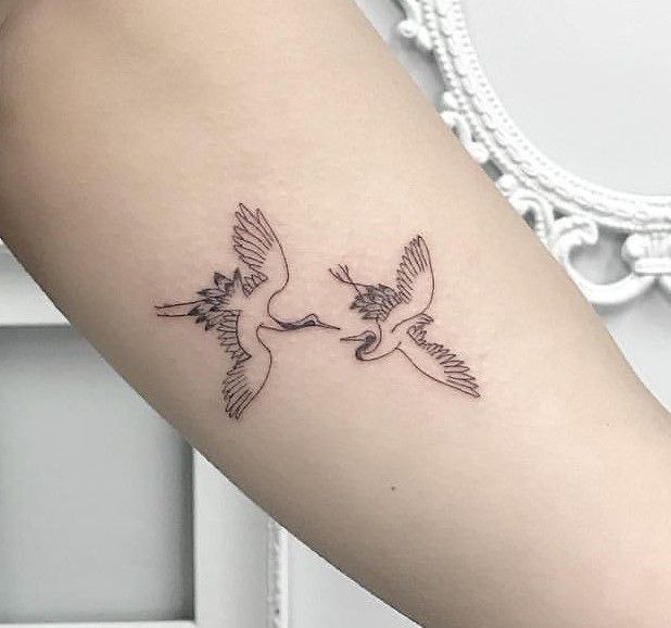 Tattoo of two storks on the arm for women