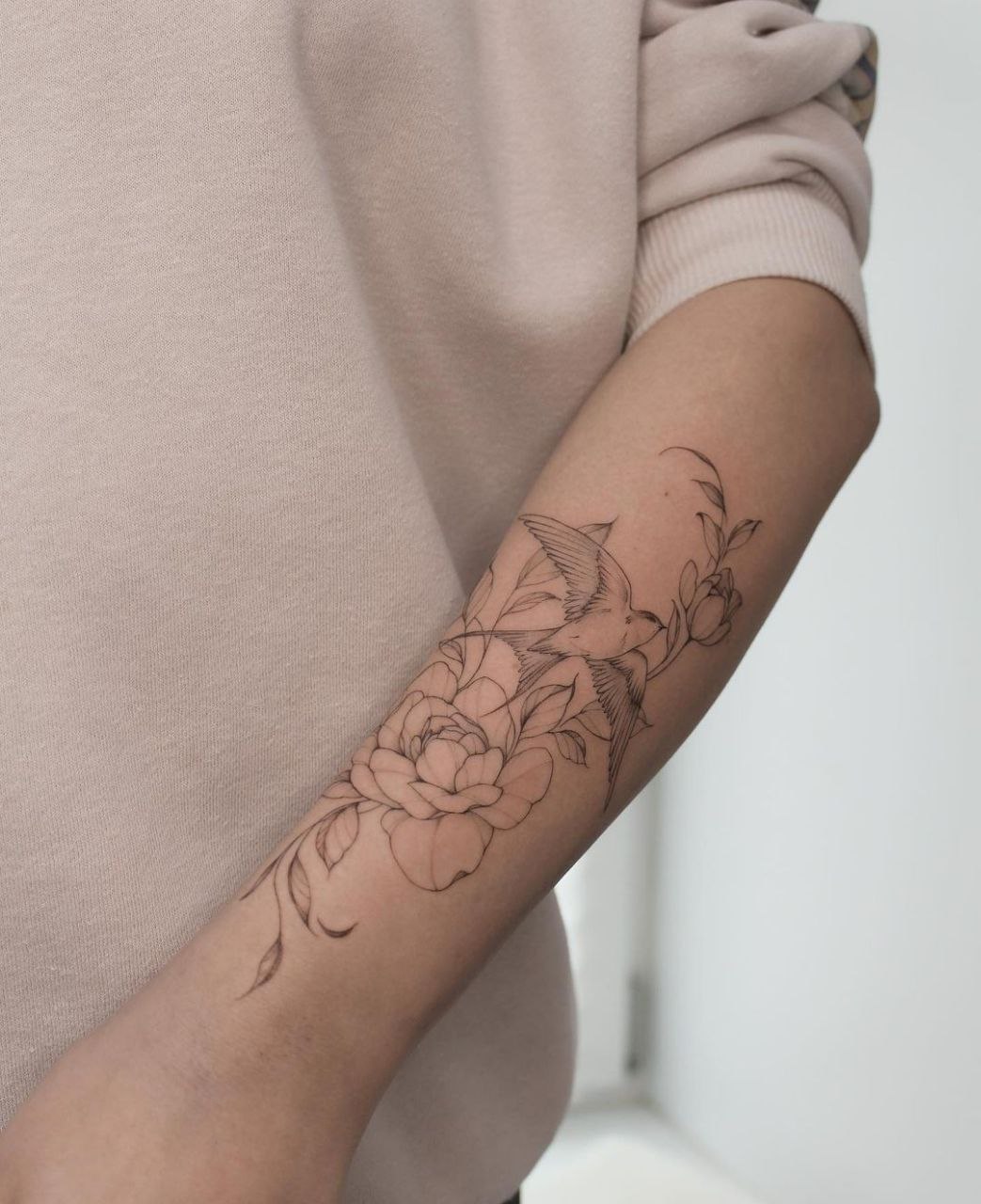 Tattoo of a swallow and flowers on the forearm for women