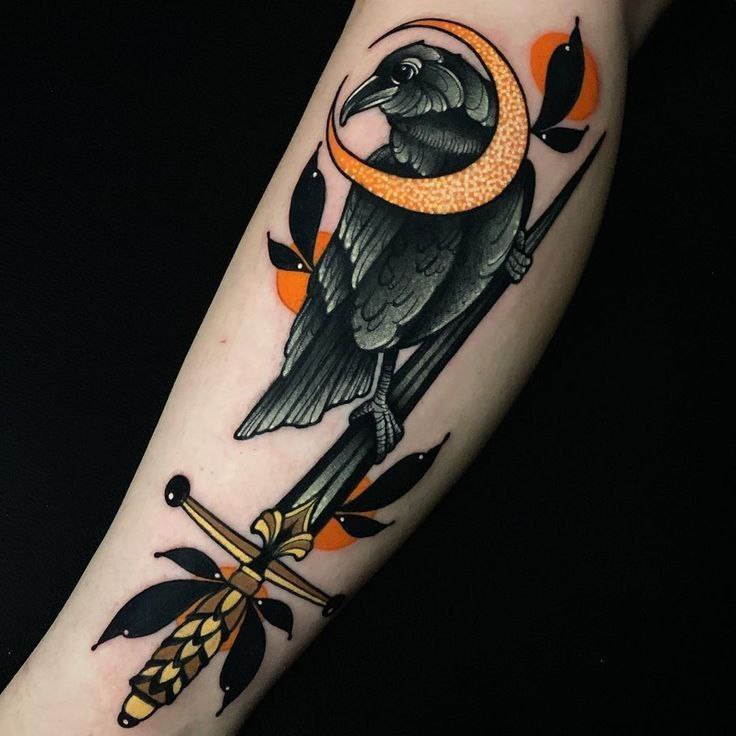 Colorful tattoo of a raven with a dagger on the arm for women