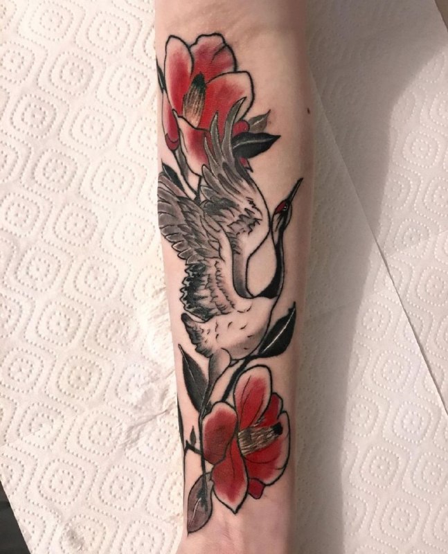 Colorful stork tattoo with flowers on the forearm for women