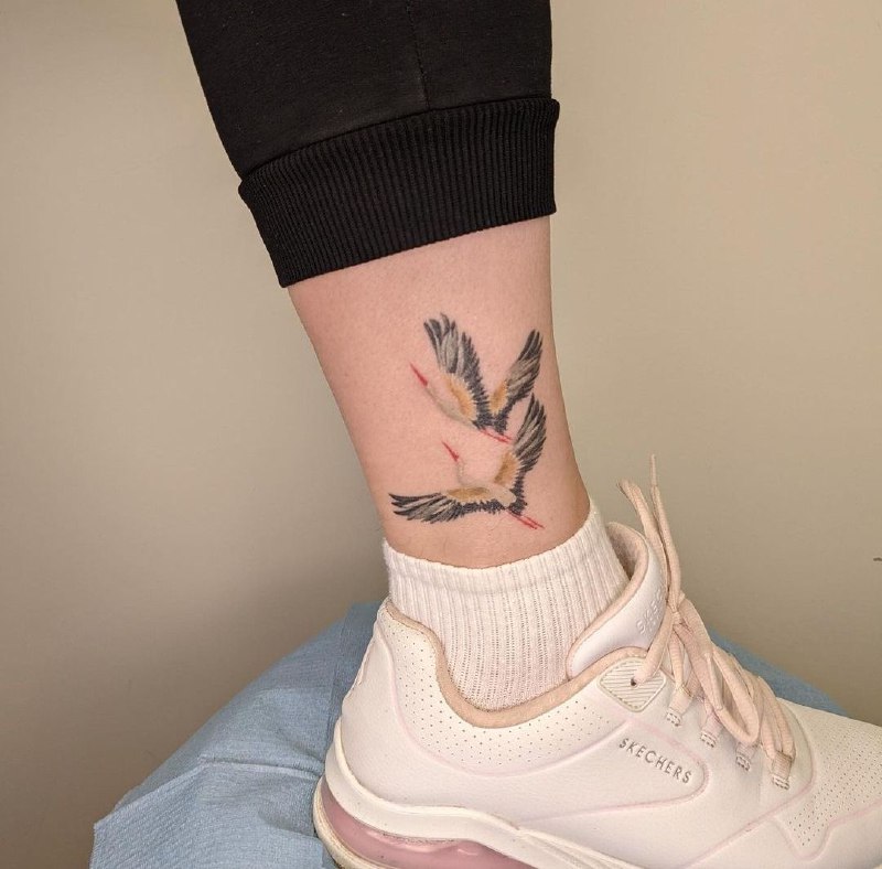 Colorful tattoo of two storks on the shin for women