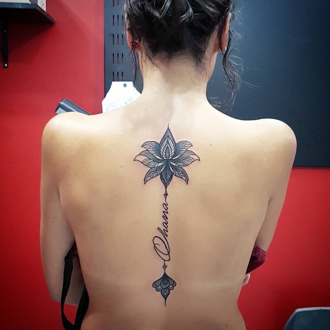 Lotus tattoo with an inscription on the spine for women