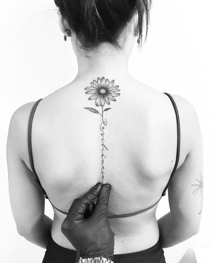 Daisy tattoo with an inscription on the spine for women