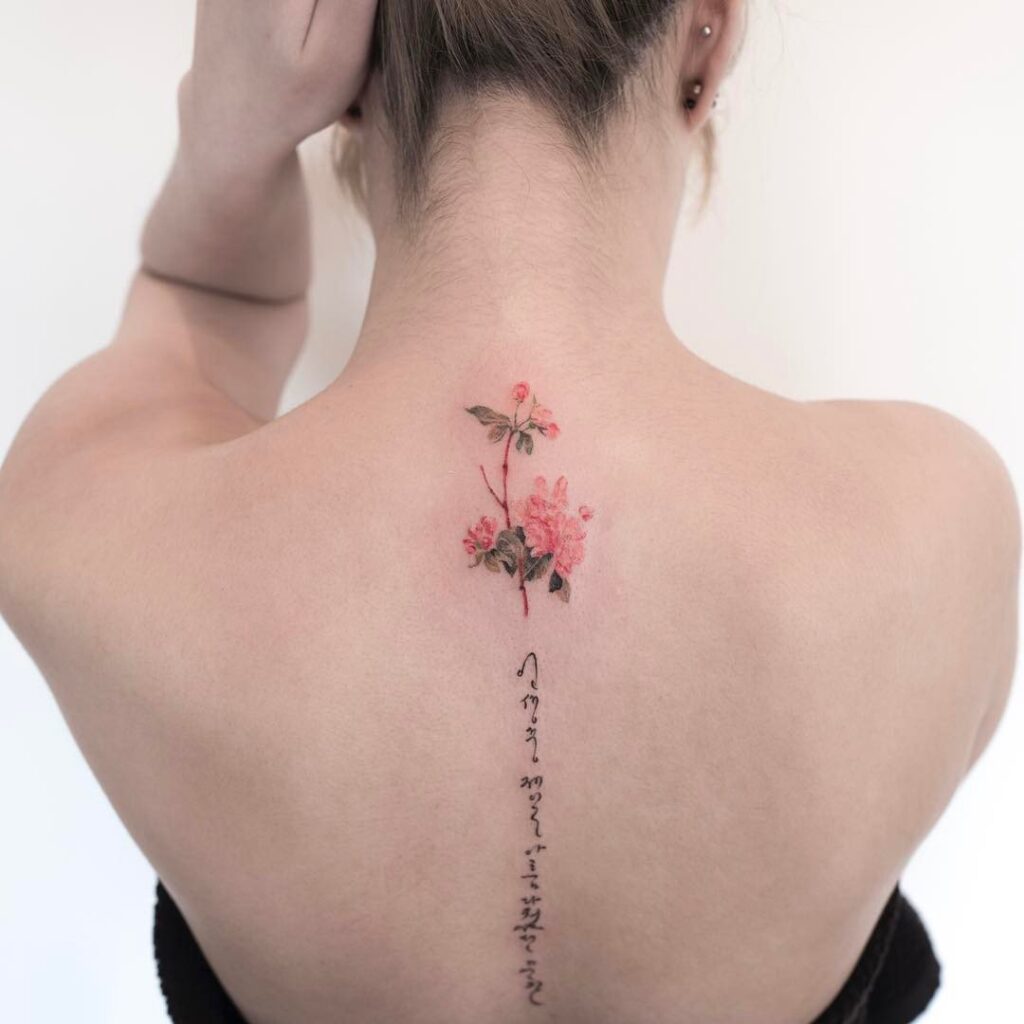 Flower tattoo with an inscription on the spine for women